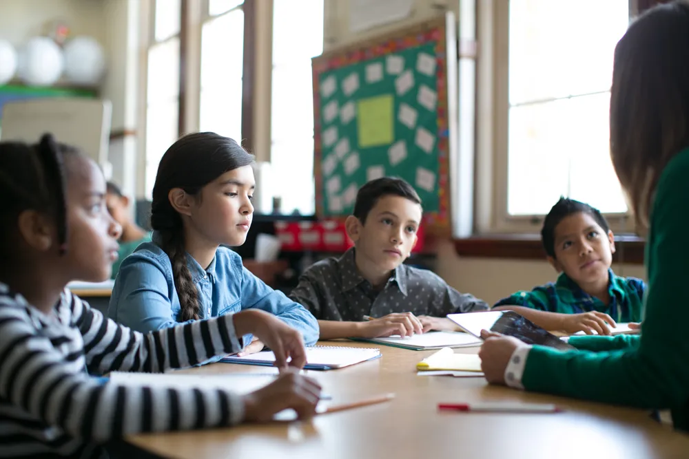 group of students at a table working listening to the teacher