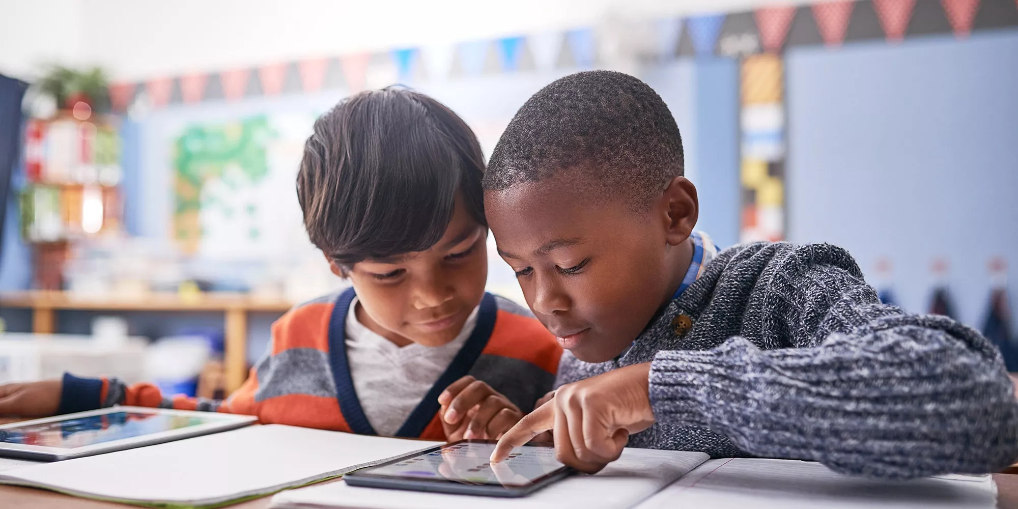 student reading along with other student on tablet in a classroom