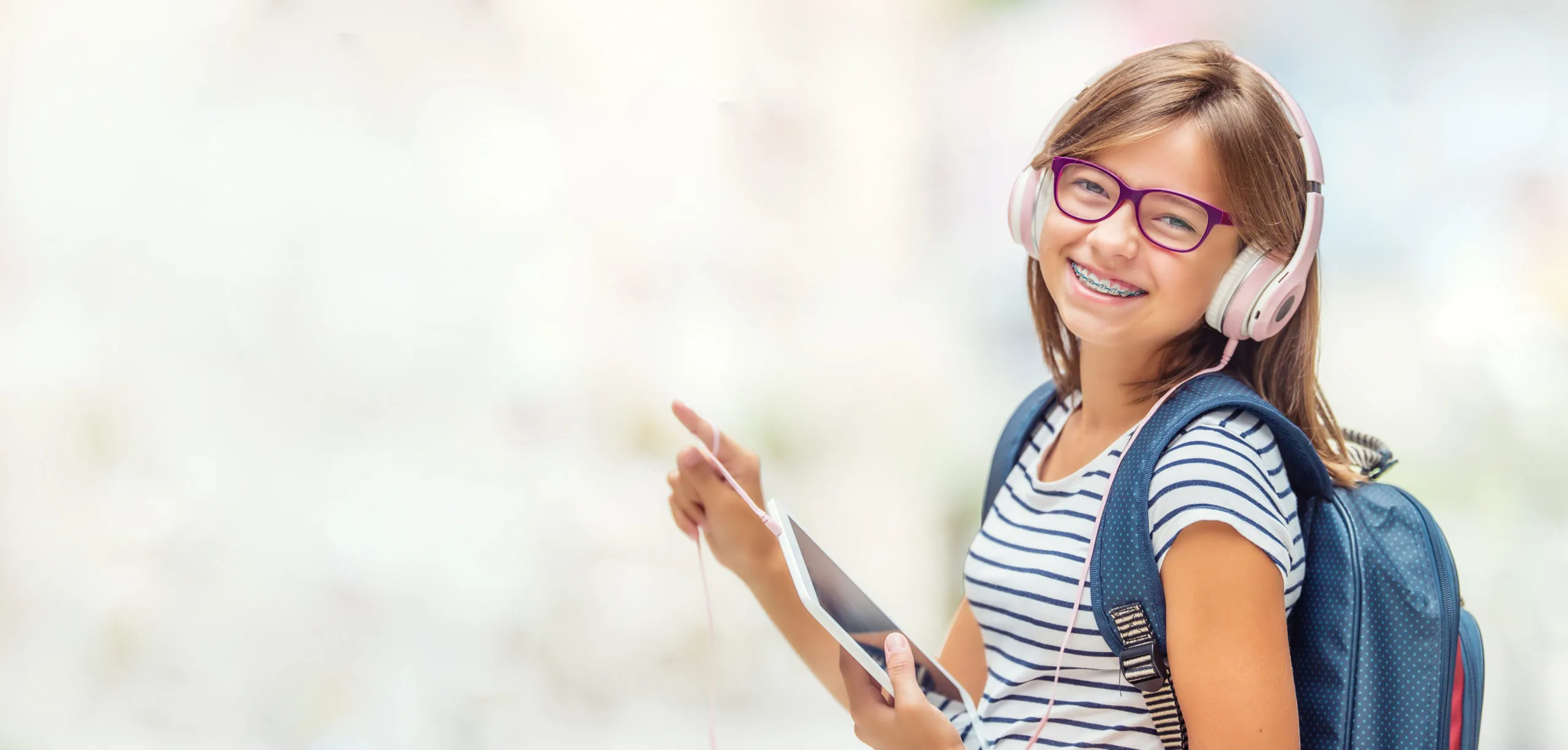 Portrait of modern happy teen school girl with dental braces glasses bag backpack headphones and tablet