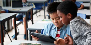 Two boys reading a digital book on a tablet in a classroom