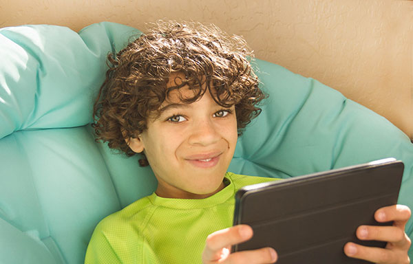Smiley boy with curly hair reading tablet