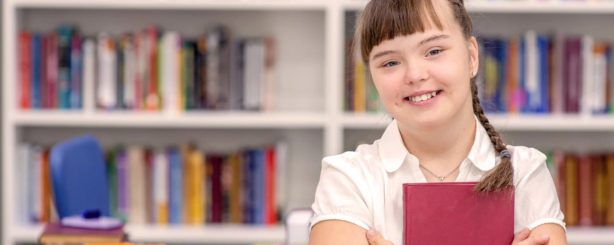 Girl holding red book standing in front of a bookcase