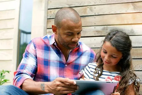 Male family member and young girl engaged in a reading activity. 