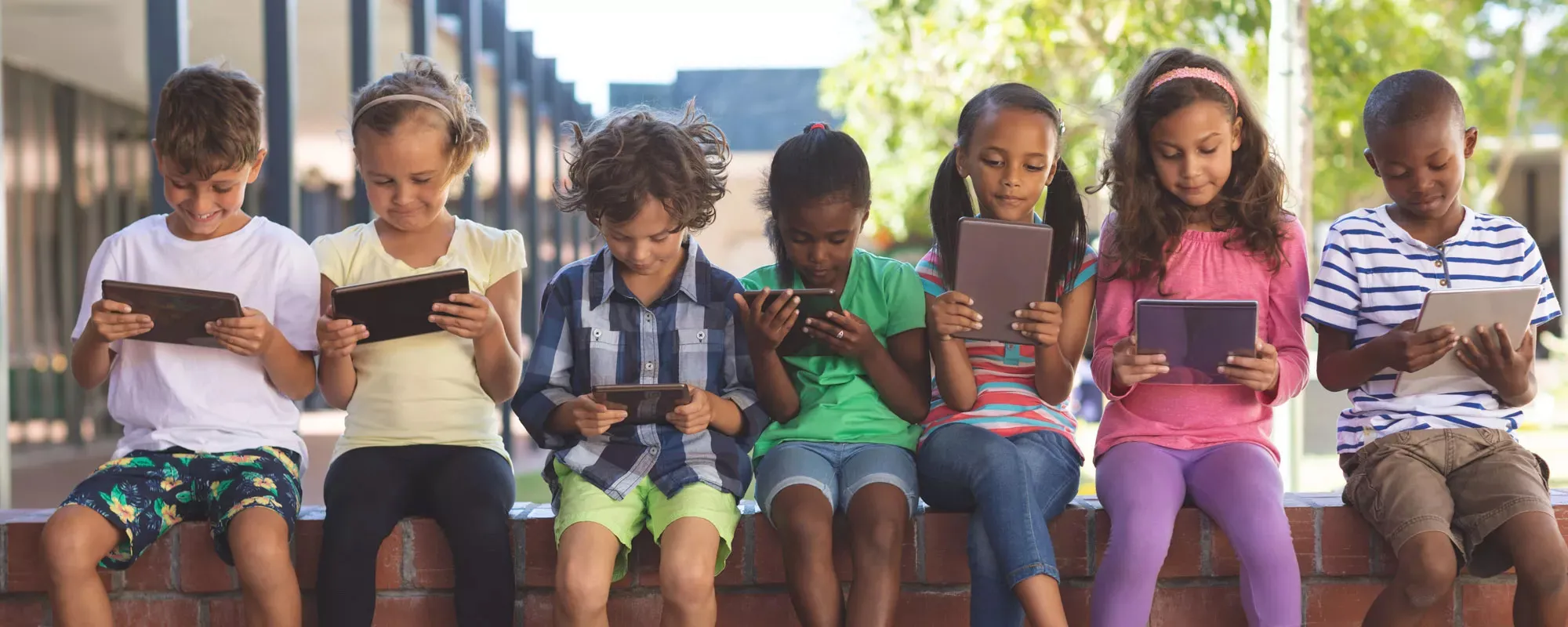 Children outside a school reading with myON on tablet computers