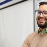 a male math teacher with fractions on a white board smiling