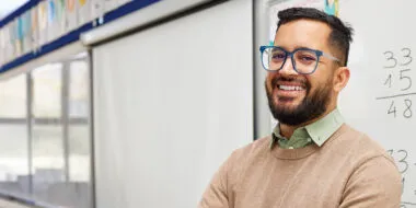 a male math teacher with fractions on a white board smiling