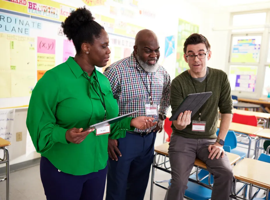 Three administrators reviewing student data on a tablet in a classroom 