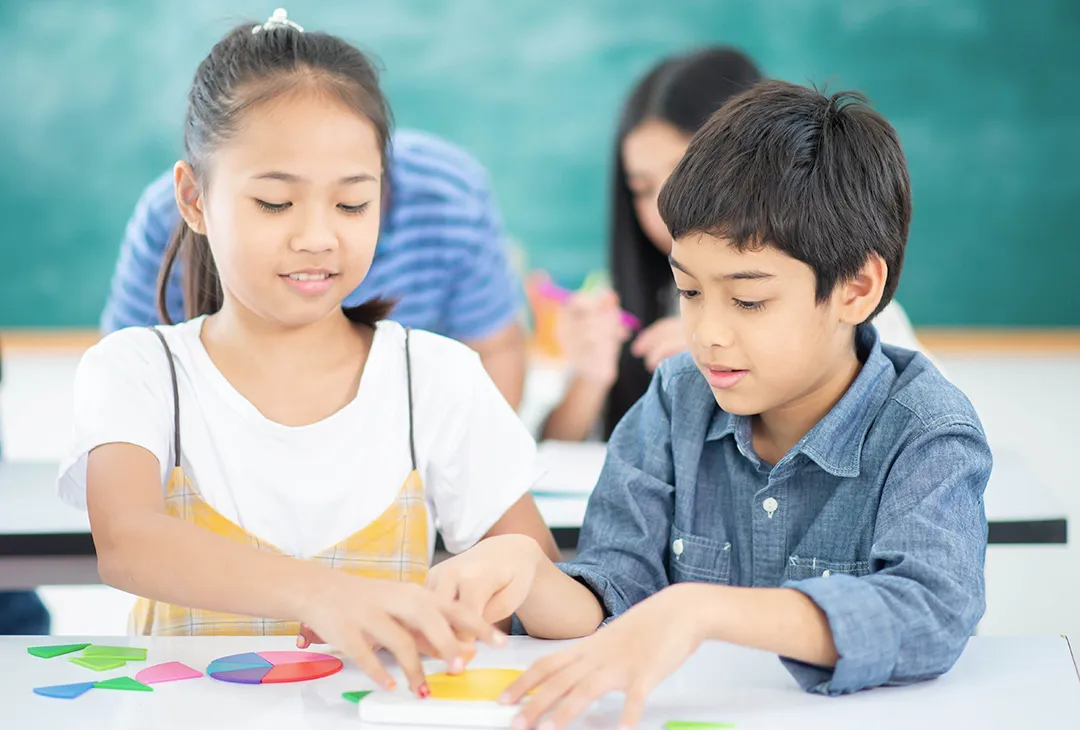 two boys in a classroom with a teacher holding books